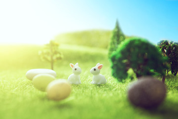 Two child rabbits toys having fun outdoor. Little bunny toys on a green meadow with colorful easter eggs. Yellow easter egg spring meadow with two white rabbit and easter eggs. Fairy tale