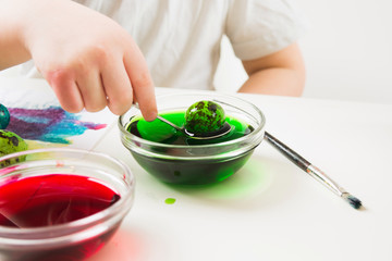 Child's hand holding spoon with green egg, child painting quail eggs for Easter
