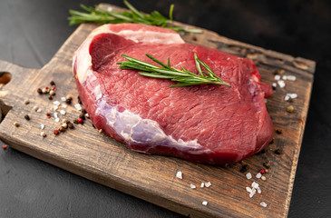 Raw fresh steak with herbs, on a cutting board, stone background, top view