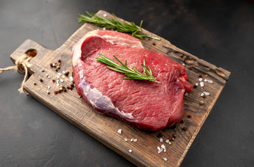 Raw fresh steak with herbs, on a cutting board, stone background, top view