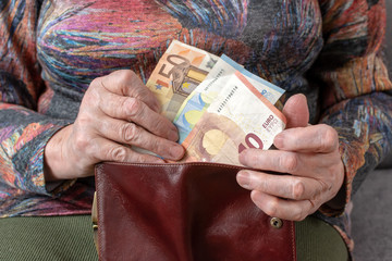 Hands of an elderly pensioner holding leather wallet with euro currency money. Concept of financial security in old age.