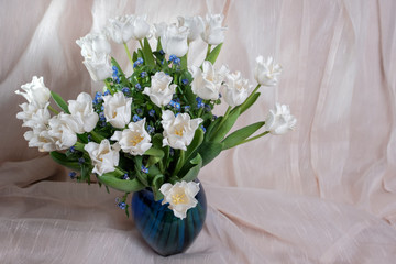 Bouquet of white tulips with forget-me-nots in a blue vase.