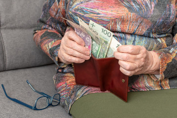 Hands of an elderly pensioner holding leather wallet with polish currency money. Concept of...