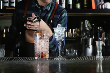 Barman pouring cocktail ingredients into mixing glass at counter in pub, closeup