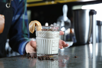 Barman holding White Russian cocktail at counter in pub, closeup