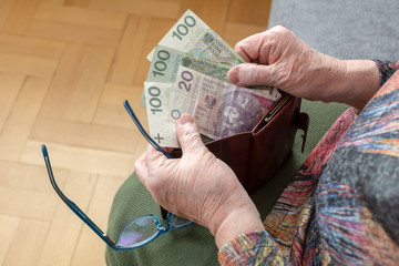 Hands of an elderly pensioner holding leather wallet with polish currency money. Concept of financial security in old age.