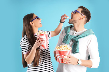 Couple with 3D glasses and tasty popcorn on color background