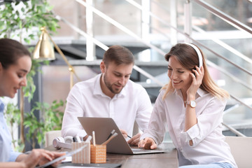 Young businesswoman with headphones, laptop and her colleagues working in office