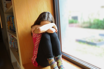 Ein Mädchen sitzt ängstlich auf der Fensterbank