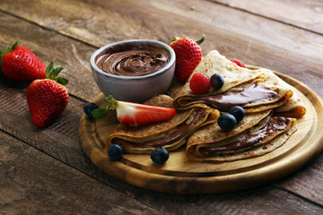 Delicious Tasty Homemade crepes with chocolate or pancakes with raspberries and blueberries on rustic wood - 255823924