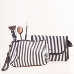 Black and white cosmetic bag among makeup brushes on a white background. Minimalistic and stylish cosmetics