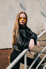 Fashion portrait pretty teenager girl in sunglasses and black rock style over city background