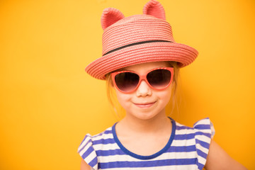 Smiling child girl in hat with ears and sunglasses on yellow background