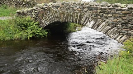 Cool mountain stream glides under stone bridge