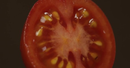 Rotate of the halves of fresh ripe cut tomato on a dark background