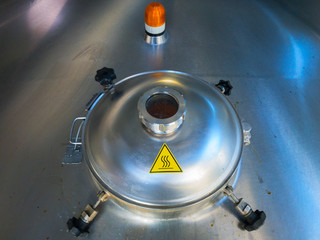 Metal door of stainless steel beer brew tank with viewing glass  with  yellow warning about...