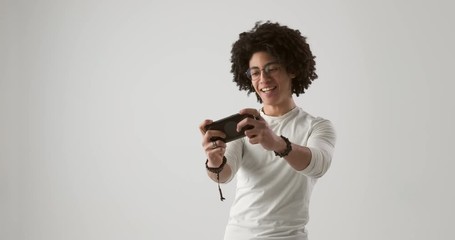Young man with curly hair playing game on mobile phone