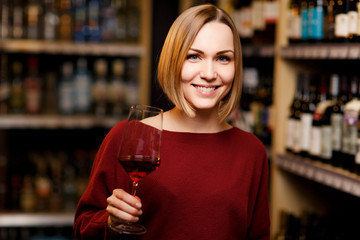 Picture of blonde with glass in hands at store with wine