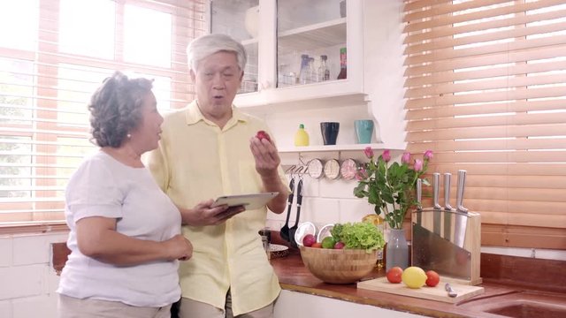 Asian elderly couple using tablet prepare ingredient for making food in the kitchen, Couple use organic vegetable for healthy food at home. Lifestyle senior family making food at home concept.