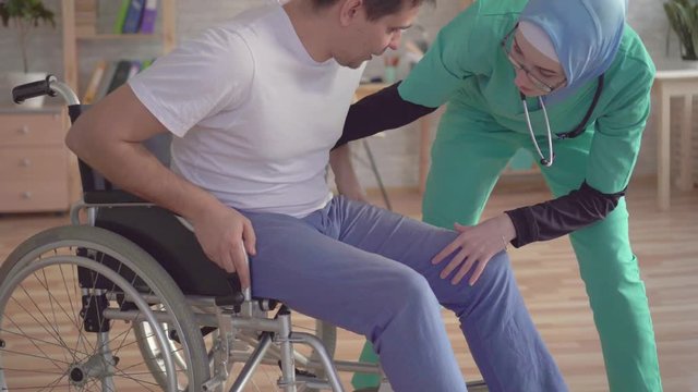 Close up of muslim nurse in hijab helps disabled person to get up from wheelchair