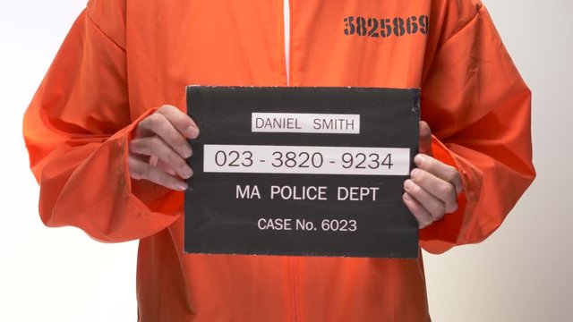 Mug shot of a jail inmate in orange suite positioning himself for the picture.