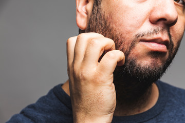 Closeup view of a man scratching beard, thoughtful gesture