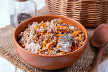 Buckwheat porridge with fish in a ceramic plate on a wooden table