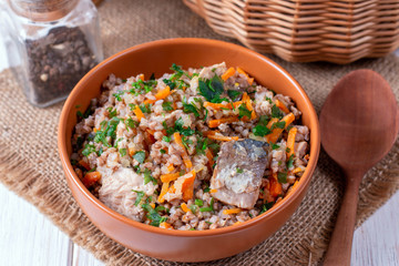 Buckwheat porridge with fish in a ceramic plate on a wooden table