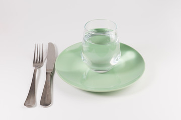 glass of water in a plate with knife and fork isolated on white background