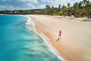 Aerial view of the running young woman on the white sandy beach near sea with waves at sunrise. Summer holiday. Top view of sporty slim girl, clear azure water. Indian Ocean. Lifestyle and sport - Powered by Adobe