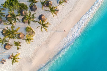 Washable wall murals Zanzibar Aerial view of umbrellas, palms on the sandy beach of Indian Ocean at sunset. Summer holiday in Zanzibar, Africa. Tropical landscape with palm trees, parasols, white sand, blue water, waves. Top view