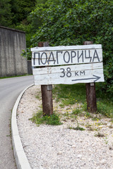 Wooden signpost with direction and distance to Podgorica city in countryside on rural asphalt road. Montenegro. Podgorica inscription in Montenegrin