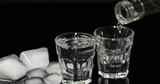 Pour vodka into shot glasses with ice cubes placed on a black background