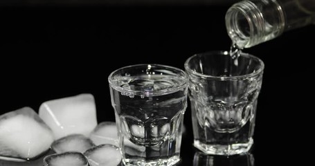 Pour vodka into shot glasses with ice cubes placed on a black background