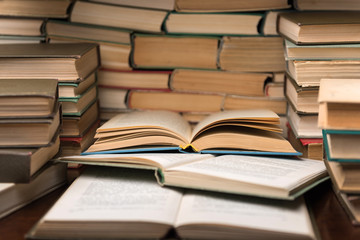 Education learning concept with open book and notebook on the table. Stack piles of books on reading desk and glasses in bookshelves background