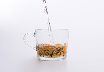 Water pouring into glass cup with tea and slices of orange isolated on white