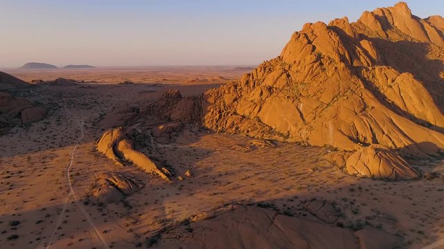 Aerial footage of Spitzkoppe mountain area. Red, bald granite peaks stand out against colorful sky and  flat surrounding plains. Popular tourist destination. Most known mountain motifs of Namibia. 4K.