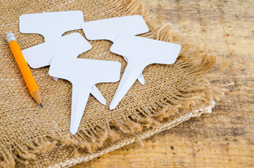 White labels-markers for plants lie on burlap, on wooden  background.