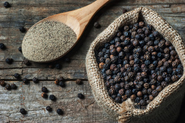heap of black pepper and black pepper powder, milled peppercorns on wooden background, dried spice...