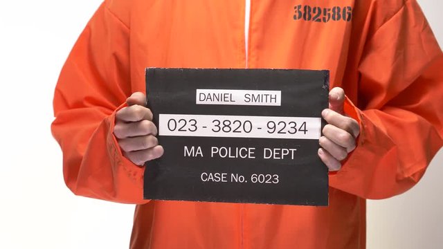 Mug shot of a jail inmate in orange suite positioning himself for the picture.
