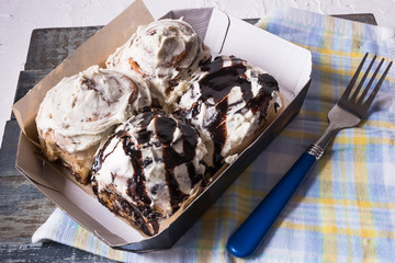 Cinnabon - cinnamon roll with cream cheese and chocolate, in a paper box, , over napkin.