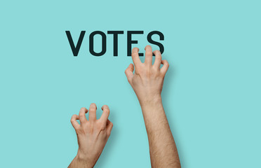 Applying for votes of voters. Hands grab the VOTES inscription on a pastel green background. The concept of elections, election promises, attempts to catch votes.