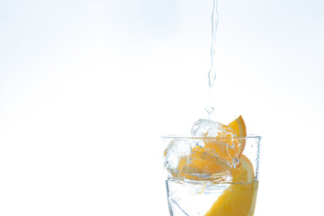 ice drink with orange and ice in the studio on a white background. a stream of water pours into the glass.