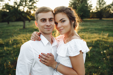 Fototapeta premium Awesome guy and girl is hugging each other and looking at the camera with smiles at sunset in the garden