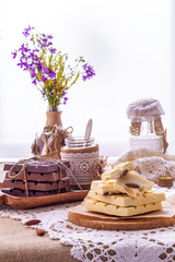 Still life with dark, milky and white chocolate bars, dishes and wild flowers bouquet of against window. Copy space.