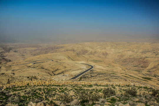 panoramic desert scenery landscape in Jordan holy mountain Nebo aerial photography with lonaly narrow curved road through dunes and horizontal board between foggy ground and blue sky, copy space - Powered by Adobe
