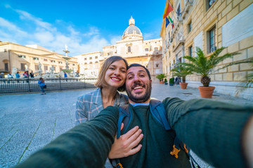 Fototapeta na wymiar happy tourist couple traveling in Palermo, Sicily and taking selfie in Famous fountain of shame on baroque Piazza Pretoria, Palermo, Sicily, Italy. Italian holidays road trip