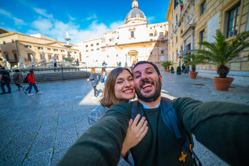 happy tourist couple traveling in Palermo, Sicily and taking selfie in Famous fountain of shame on baroque Piazza Pretoria, Palermo, Sicily, Italy. Italian holidays road trip