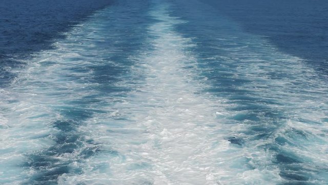 White traces on blue sea water behind the ship