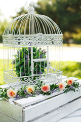 Festive rustic style decorations fresh flowers and white birdcage on a wooden box. Sunny summer day